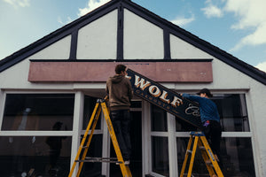 Scottish signwriter Ross Hastie and his apprentice fitting the hand-painted Bear&Wolf shop sign in Garmouth