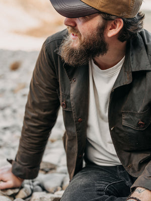 Cairn British-made waxed cotton overshirt in Raven worn outdoors on a rocky Scottish shoreline