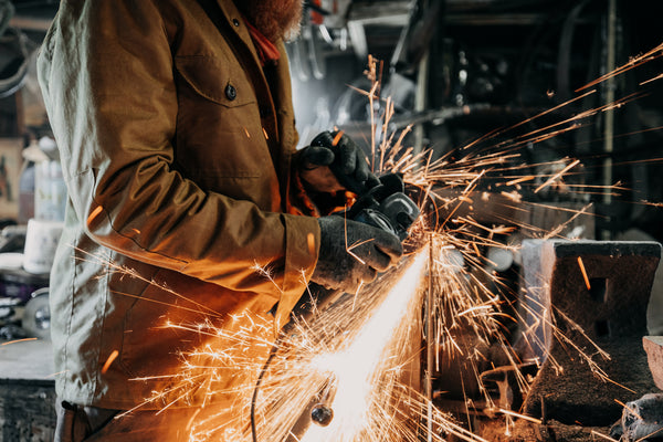 Cairn British-made waxed cotton overshirt in Whisky worn by a blacksmith grinding metal at Flett Forge
