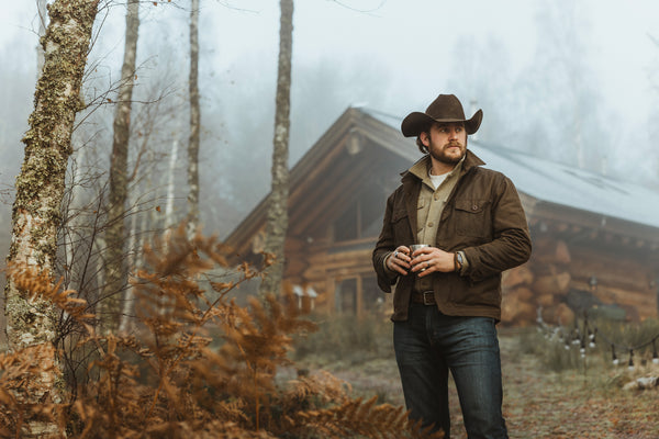 Bear&Wolf founder Jake wearing the Cairn Overshirt in Raven, drinking coffee at a Scottish log cabin.