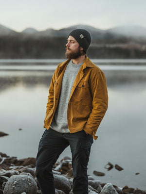 Bear&Wolf Co-Founder Bill Spurr by a Scottish loch, wearing the Whisky Cairn Overshirt, Moorland Jumper and the Ironstone Gray Lambswool Beanie.