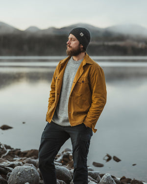 Bear&Wolf Co-Founder Bill Spurr by a Scottish loch, wearing the Whisky Cairn Overshirt, Moorland Jumper and the Ironstone Gray Lambswool Beanie.