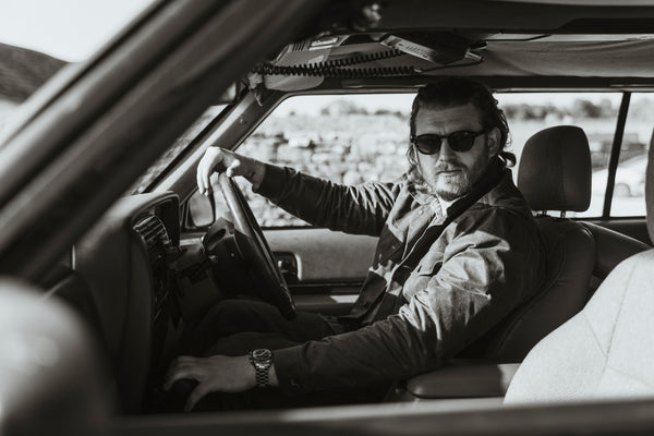 A black and white image of Bear&Wolf founder Jake Green modelling the stac in kelp green on a photoshoot in the cotswolds whilst driving a classic Jeep.