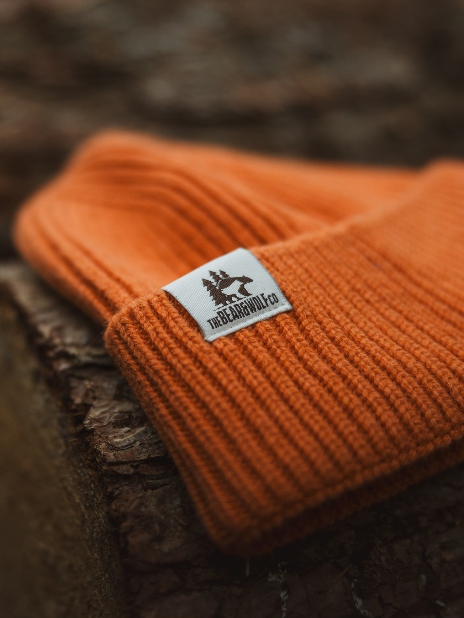 Bear&Wolf Accessories - A Lambswool Beanie in Ember Orange placed on a wooden log.