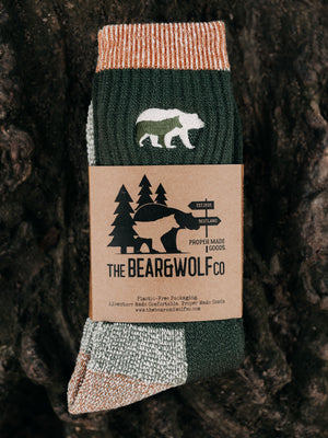 A pair of Bear&Wolf Merino Rambler Socks in Pine, placed on a tree log.