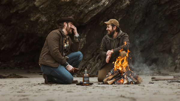 Bear&Wolf founders Jake and Bill wearing Cairn Overshirts in Raven, with Bill in a Wax Cap, at a beach campfire on the Scottish island of Shetland.