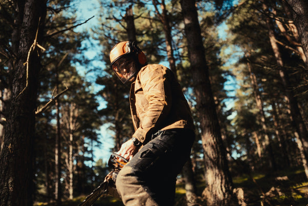 A logger operating a chainsaw in a forest whilst wearing a Stac in saddle brown and safety gear.