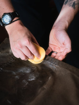 Close-up of Old Faithful No.01 wax treatment being applied with a sponge to the seams and waxed cotton fabric of a Cairn Overshirt.