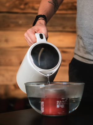Pouring hot water from a kettle into a glass bowl to soften Old Faithful No.01 wax treatment before reproofing a Cairn Overshirt.