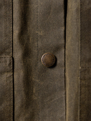 Close-up of The Stac waxed cotton jacket in Kelp Green showing the branded metal button.
